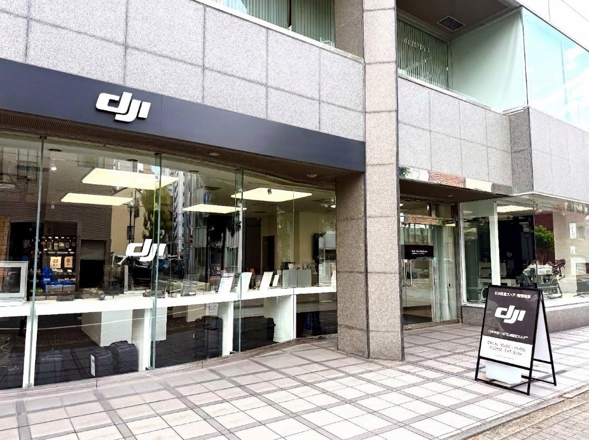 DJI認定ストア福岡博多の外観。ガラス張りの店舗の上にDJIのロゴサインが掲げられ、歩道に営業案内の看板が置かれている